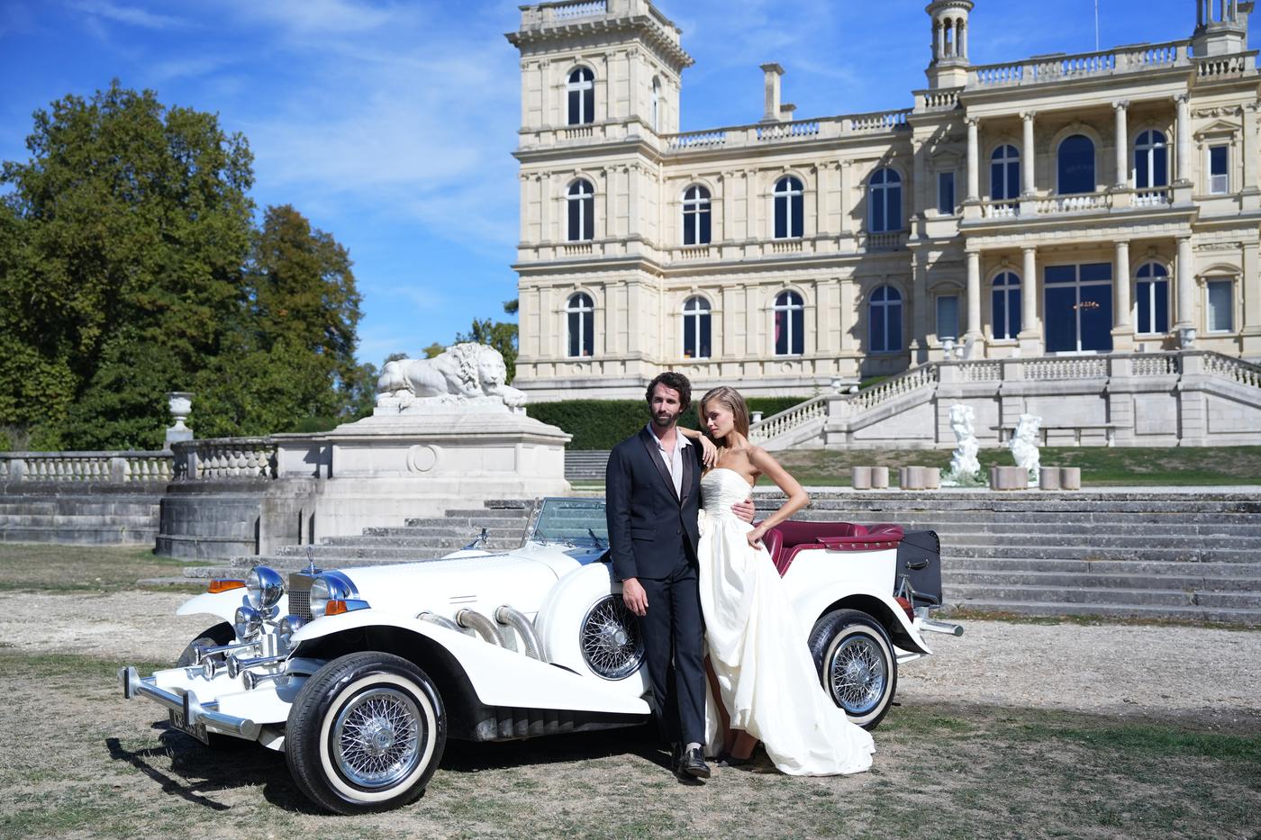 Teaser de mariage : les mariés posent contre une voiture ancienne devant la façade du château