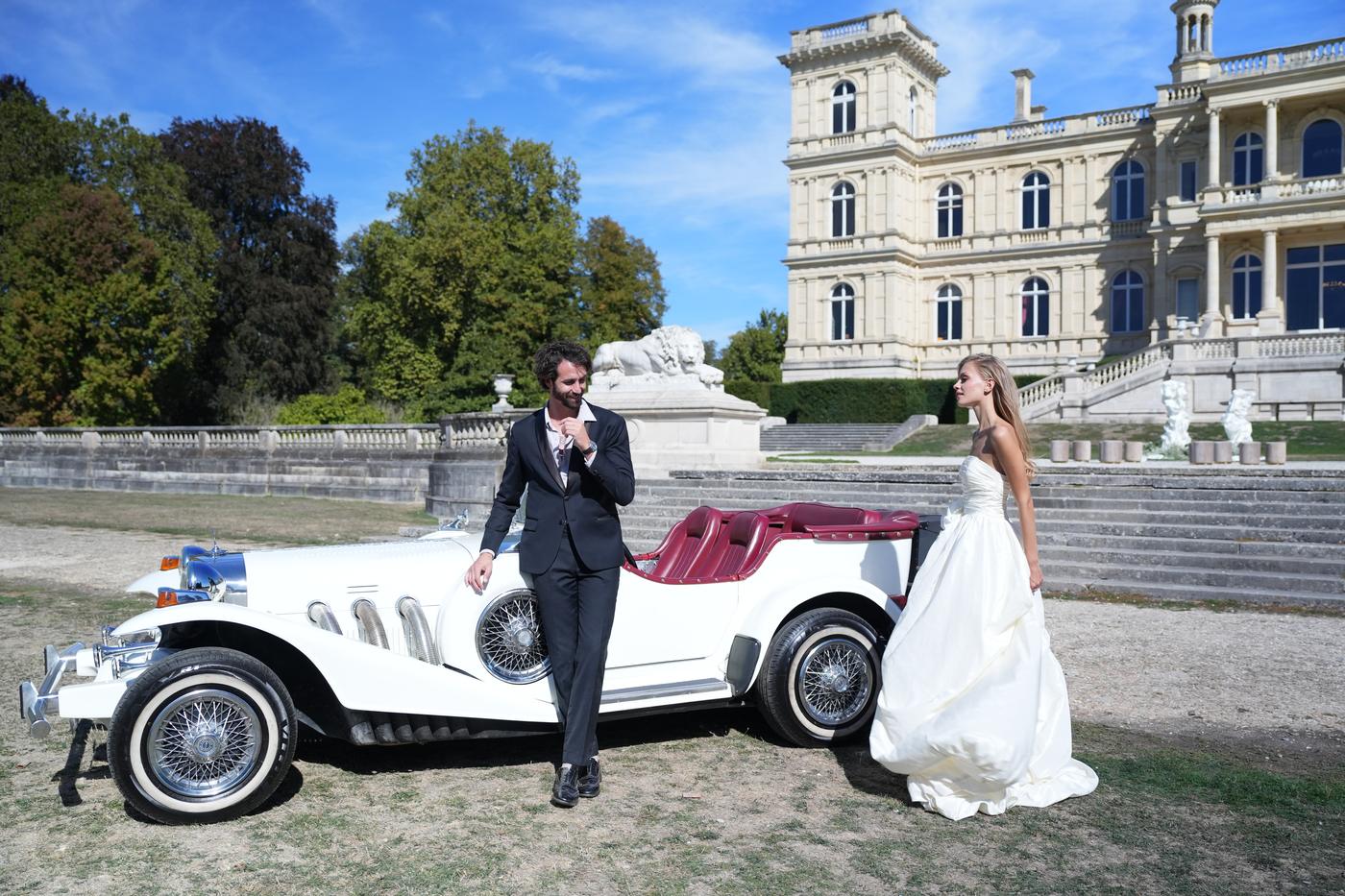 Film de mariage : le marié sourit, appuyé sur la voiture, pendant que la mariée s'avance